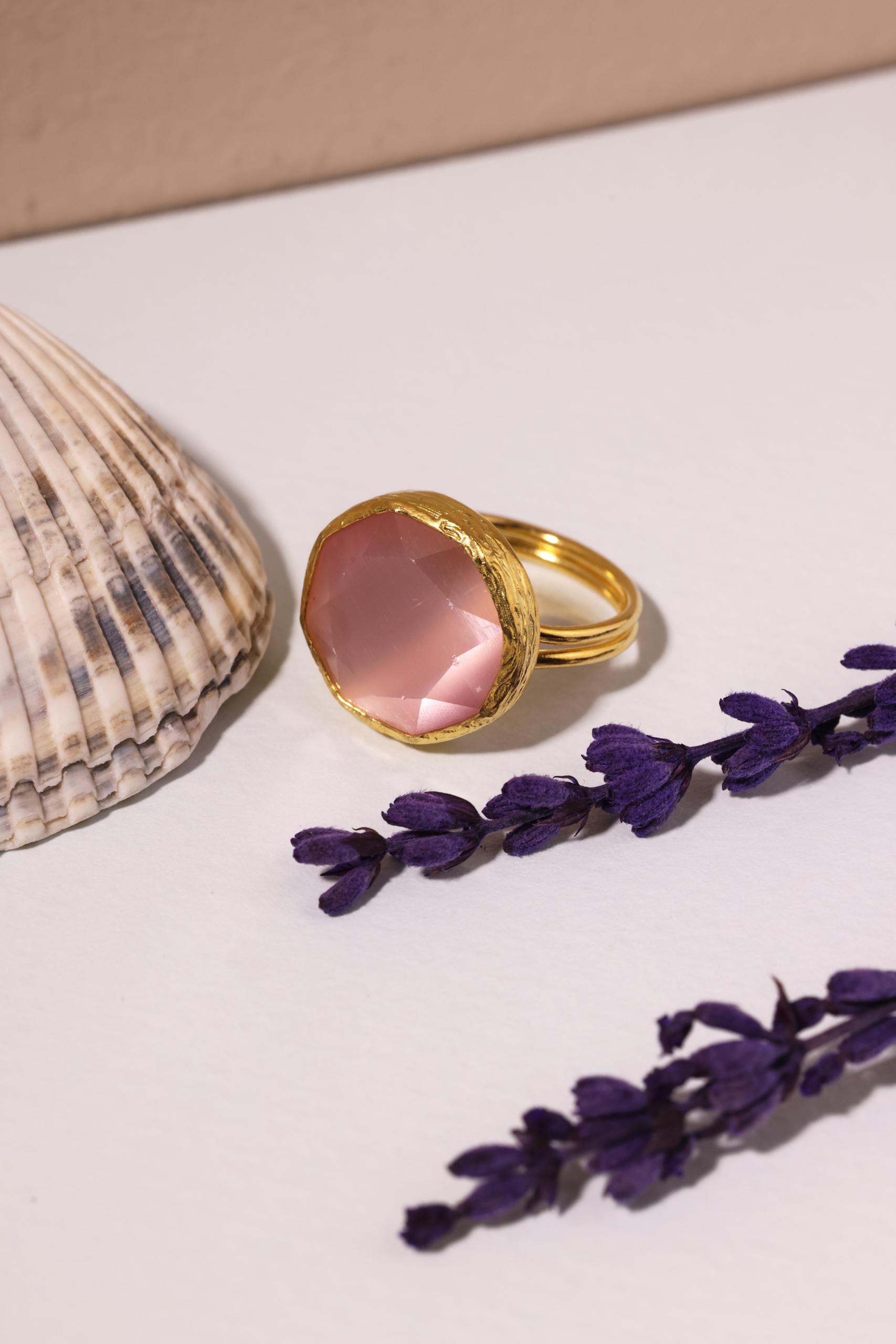 Beautiful gold ring with pink gemstone, styled with lavender and seashell.